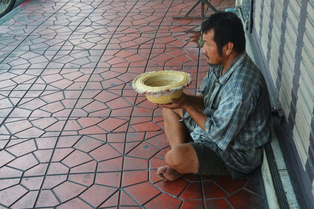 beggar sitting in the street holding a hat upside down to collect money